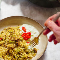 Biryani i skål med raita med en hånd som dypper en gaffel i maten