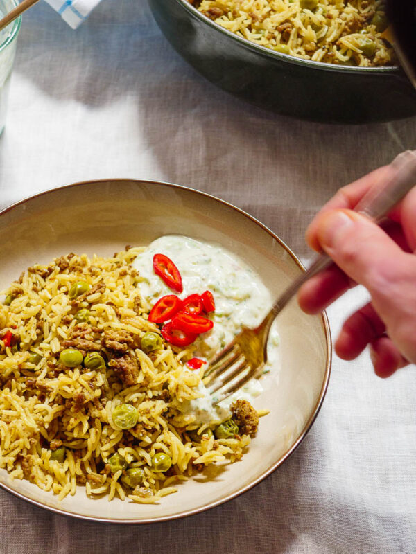 Biryani i skål med raita med en hånd som dypper en gaffel i maten