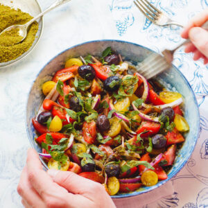 Tomatsalat med oliven og za'atar fra siden med hender som holder salatbollen
