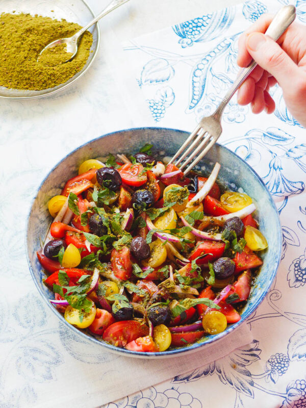 Tomatsalat med oliven og za'atar fra siden med gaffel som forsyner seg