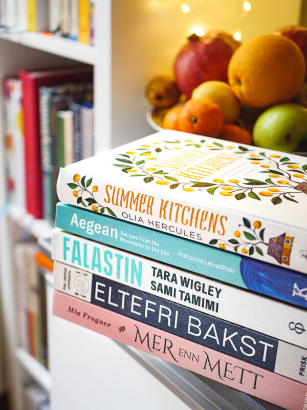Anbefalte kokebøker liggende på kjøkkenbenk med bokhylle i bakgrunn