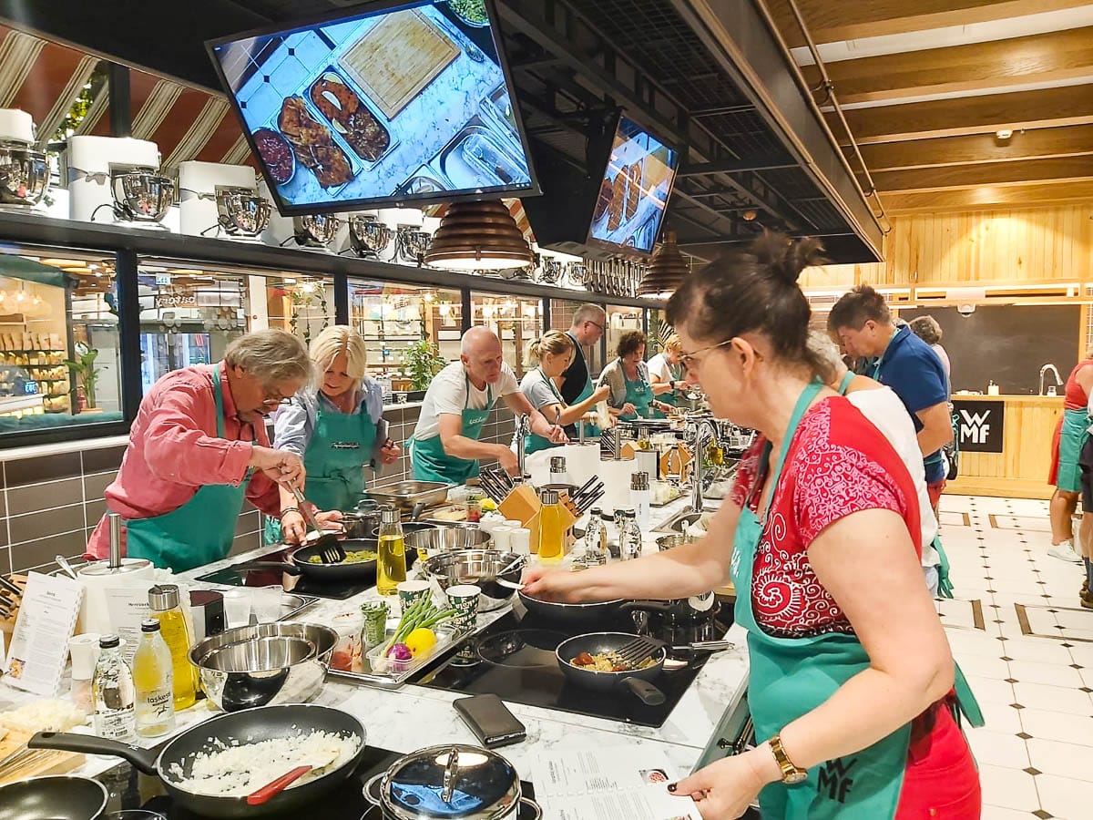 Deltakere med forkle lager mat på profesjonelt kurskjøkken.