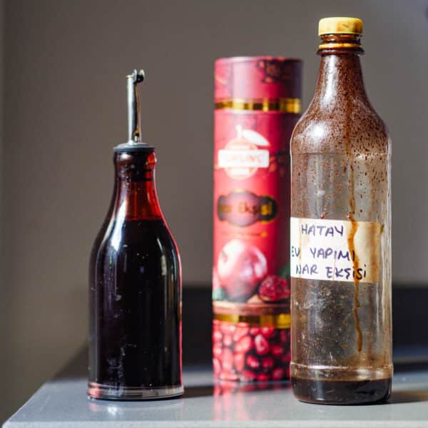 Flasker med granateplesirup. En mørkebrun beholder, en plastflaske som er nesten tom og et fargerikt, dekorert rør lagd for å inneholde en flaske granateplesirup.